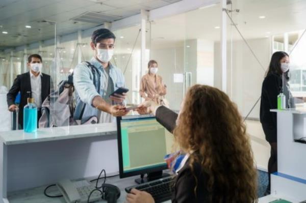 A male airline passengerwith mask is handing over his passport at the airline counter check in through an acrylic barrier for disease prevention coro<em></em>navirus or covid-19 at airport for New normal travel