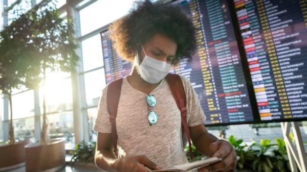male traveler wearing a facemask at the airport with the flight schedule